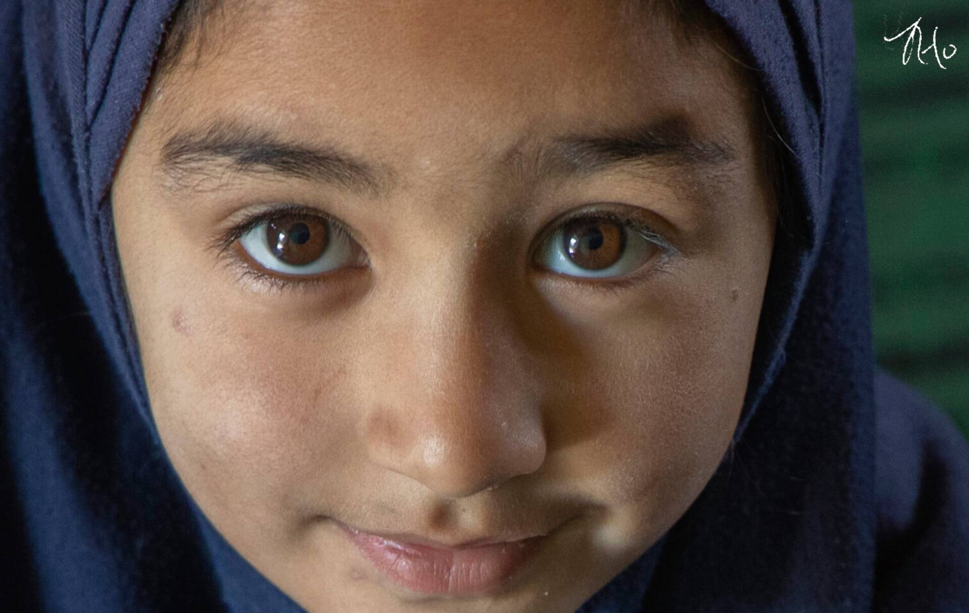 A young girl wearing a hijab is looking at the camera.