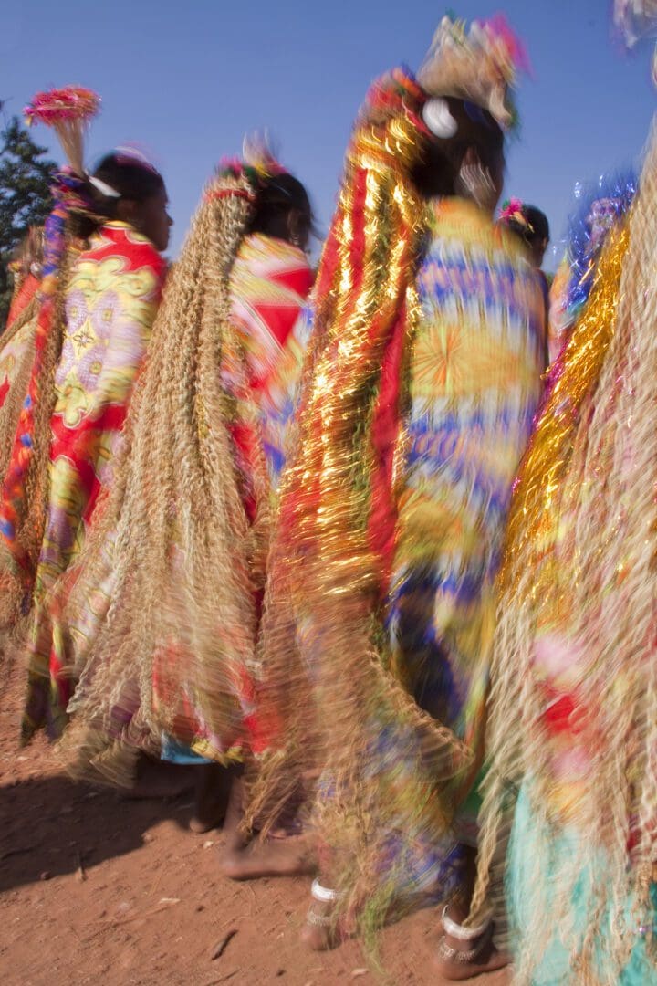 A group of women dressed in colorful clothing walking down a dirt road.