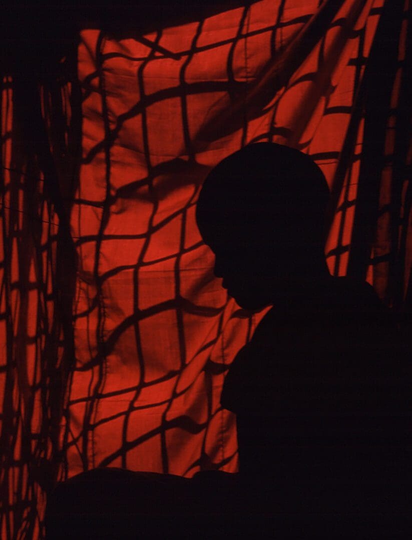 A silhouette of a child in front of a red curtain.