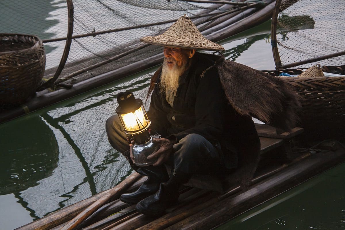 A man sitting on a boat holding a lantern.