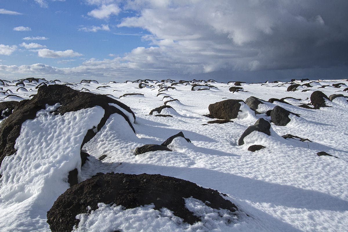 A group of rocks covered in snow under a cloudy sky.