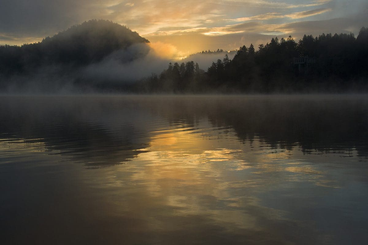 A misty sunrise over a lake with mountains in the background.