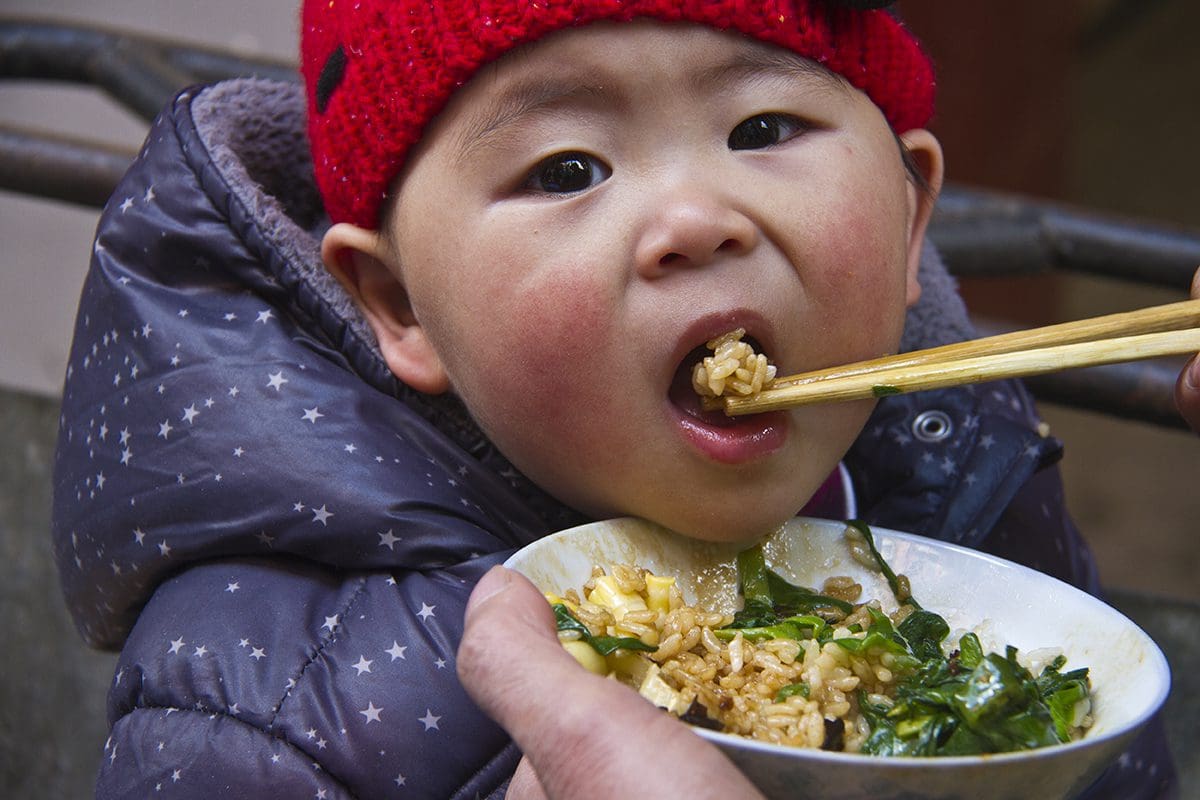 A child is eating a bowl of food with chopsticks.