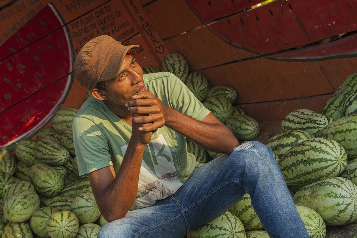 A man sitting in front of a bunch of watermelons.