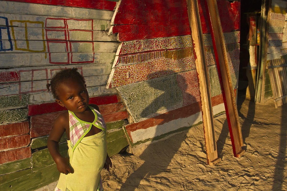 A young girl standing in front of a shack.
