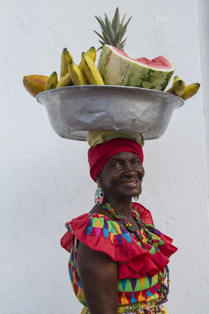 A woman with a platter of fruit on her head.