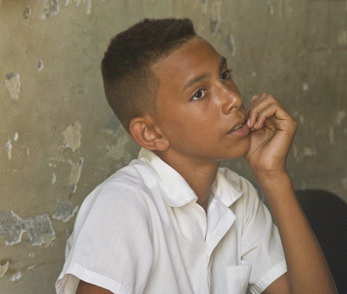 A boy in a white shirt with his hand on his chin.