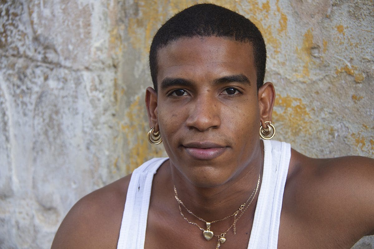 A young man wearing a white tank top and ear studs.