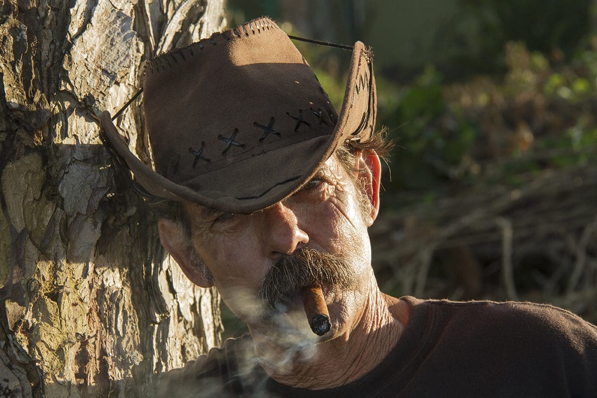 A man wearing a cowboy hat smoking a cigar.