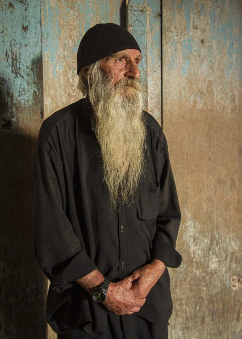 An old man with a long beard standing in front of a door.