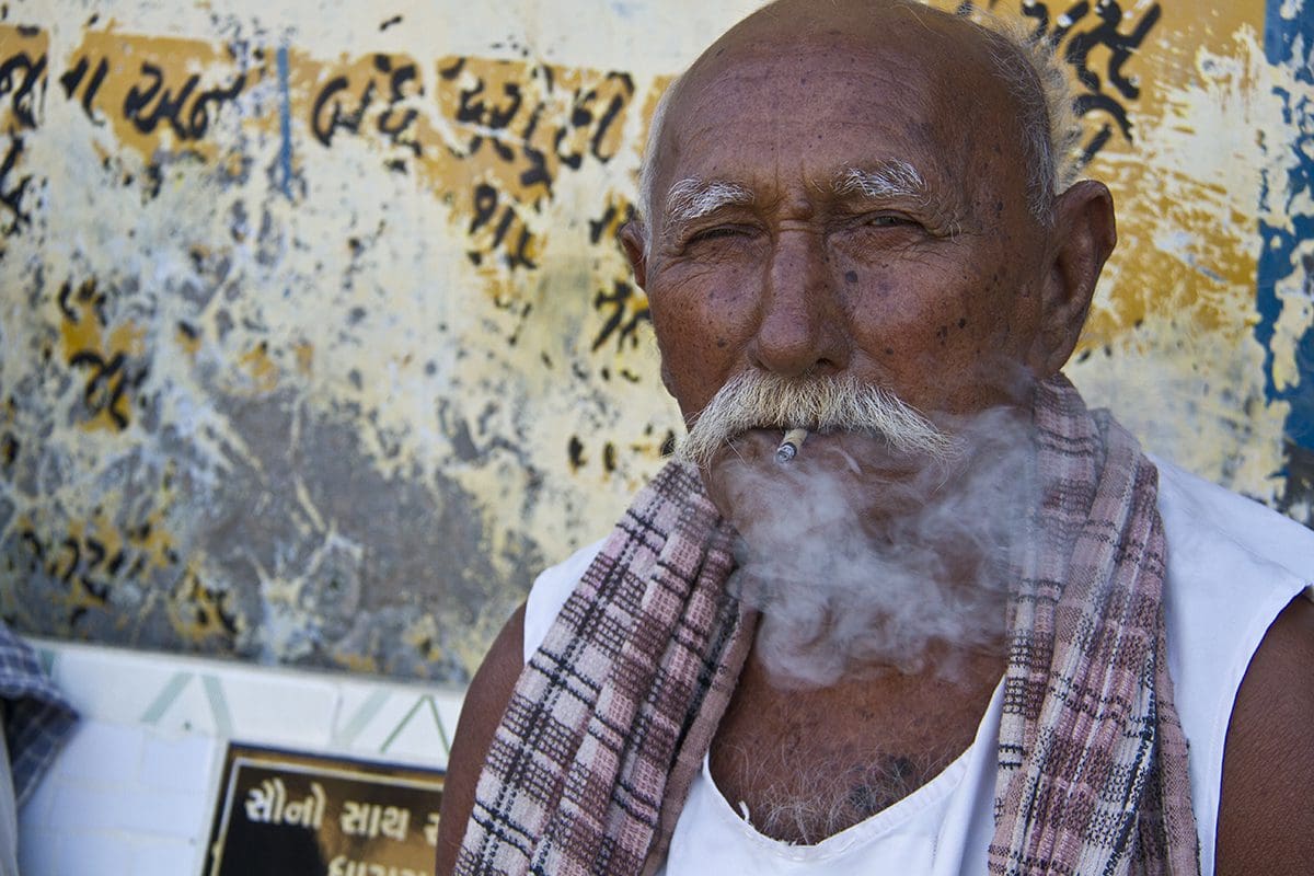 An indian man smoking a cigarette in front of a wall.