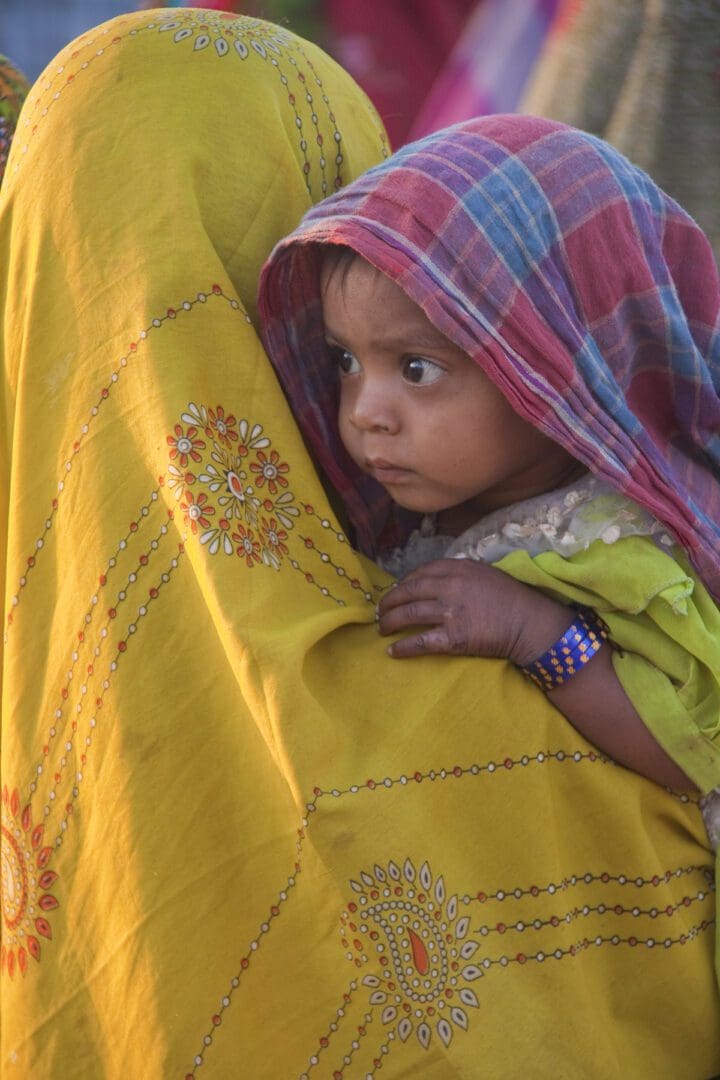 A woman in a yellow sari with a baby in her arms.