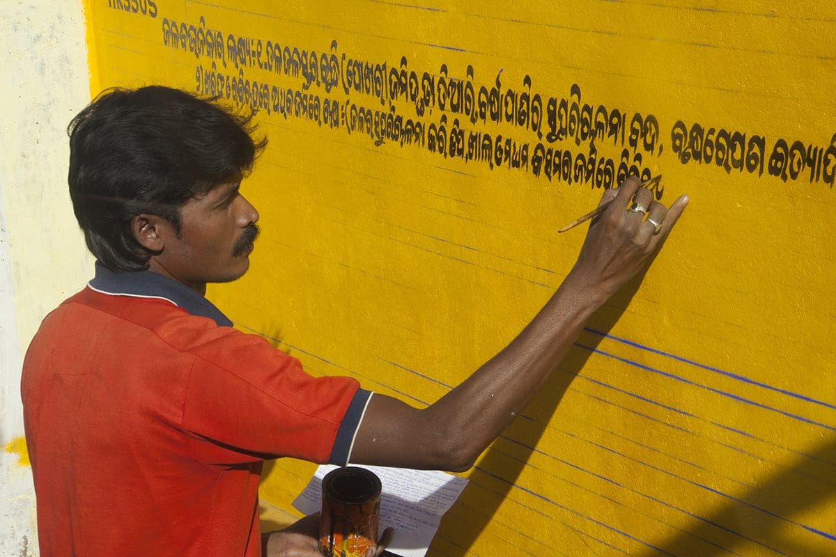 A man writing on a yellow wall.