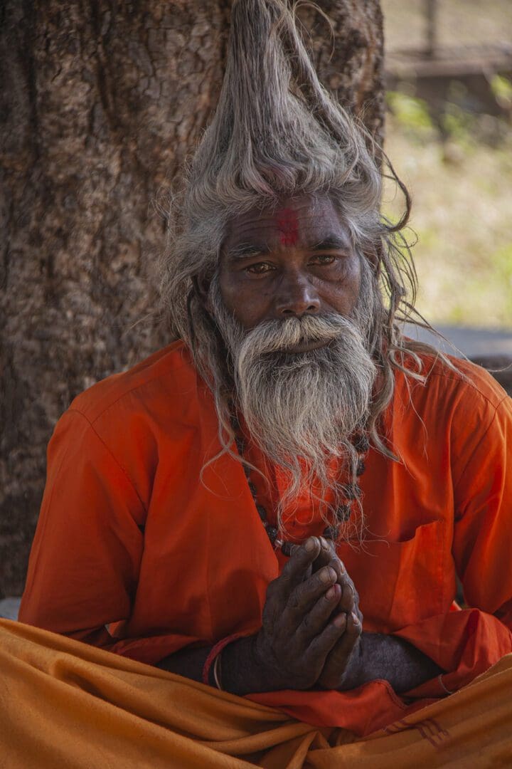An indian man with a beard sitting under a tree.