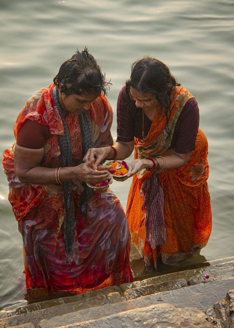 Two women in saris standing next to a body of water.