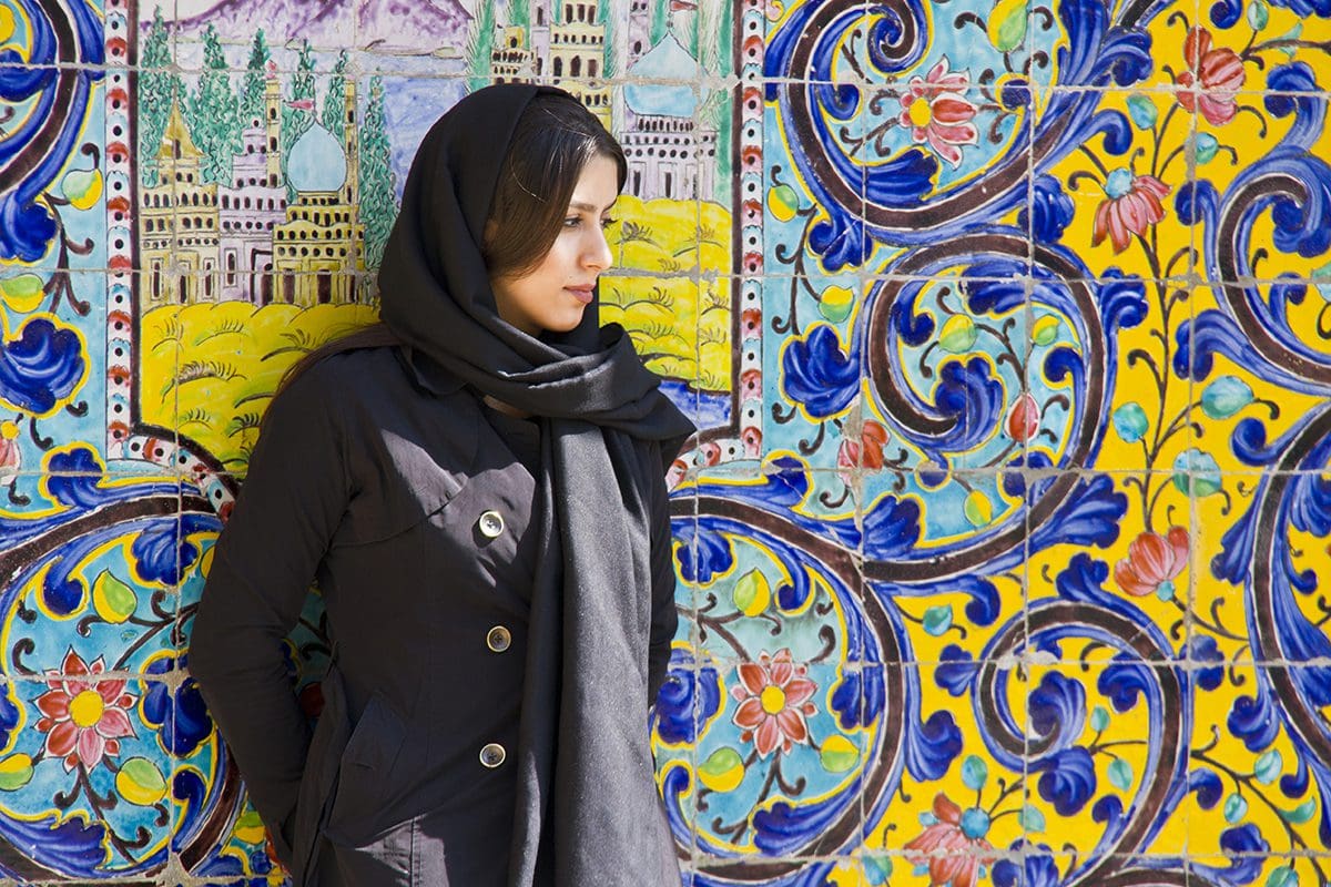 A woman in a black scarf leaning against a colorful wall.