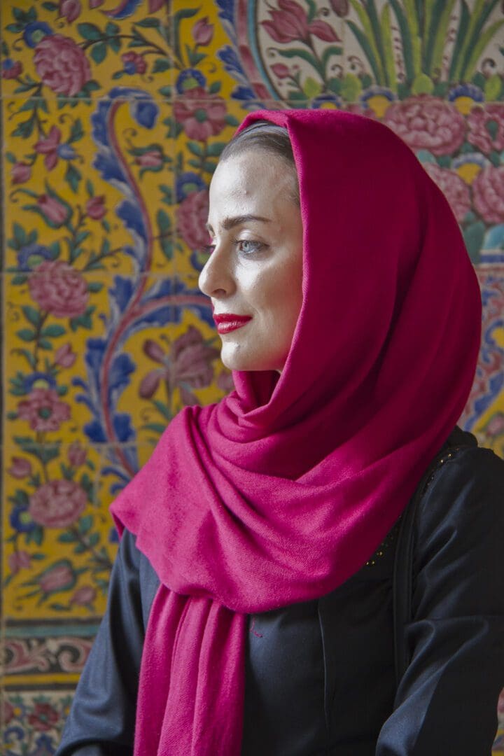 A woman wearing a red hijab in front of a colorful wall.