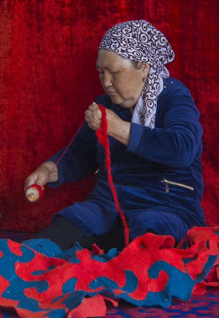A woman is knitting on a red rug.