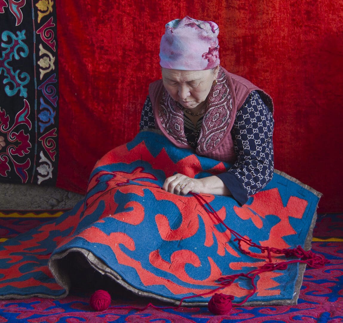 A woman is making a rug on the floor.