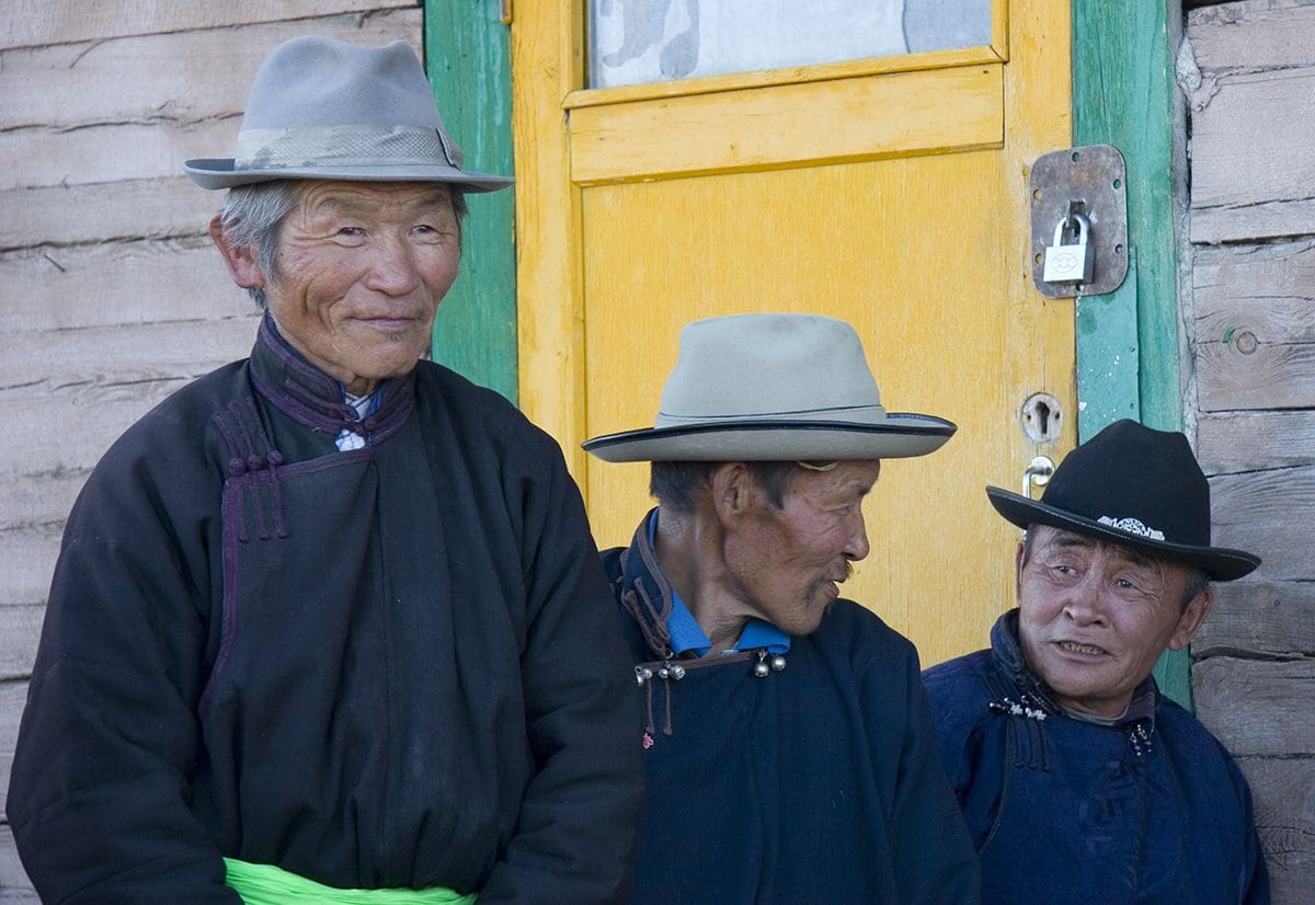 Three men in hats standing in front of a yellow building.