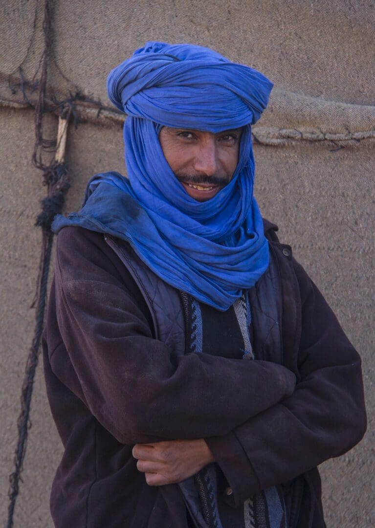 A man wearing a blue turban in front of a tent.