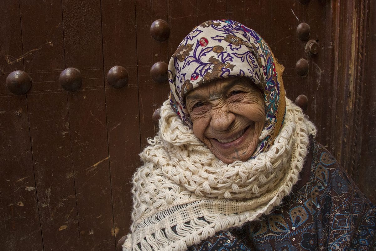 An old woman wearing a scarf and smiling.