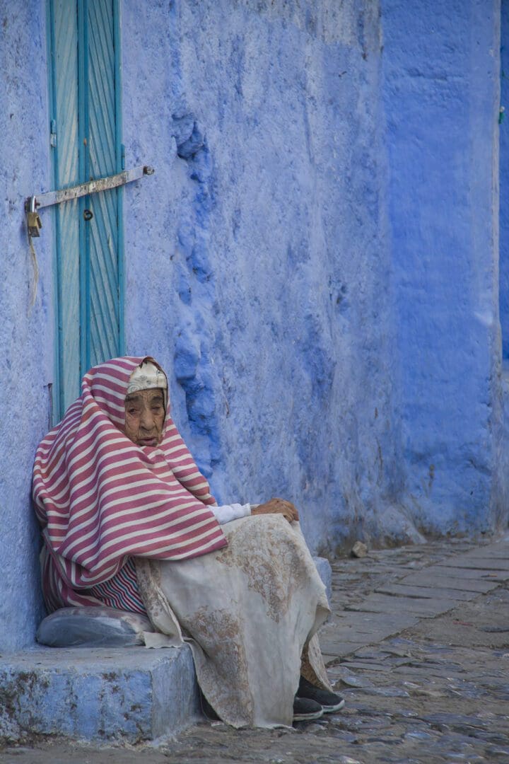A woman sitting on the steps of a blue building in chefchaouen, morocco.
