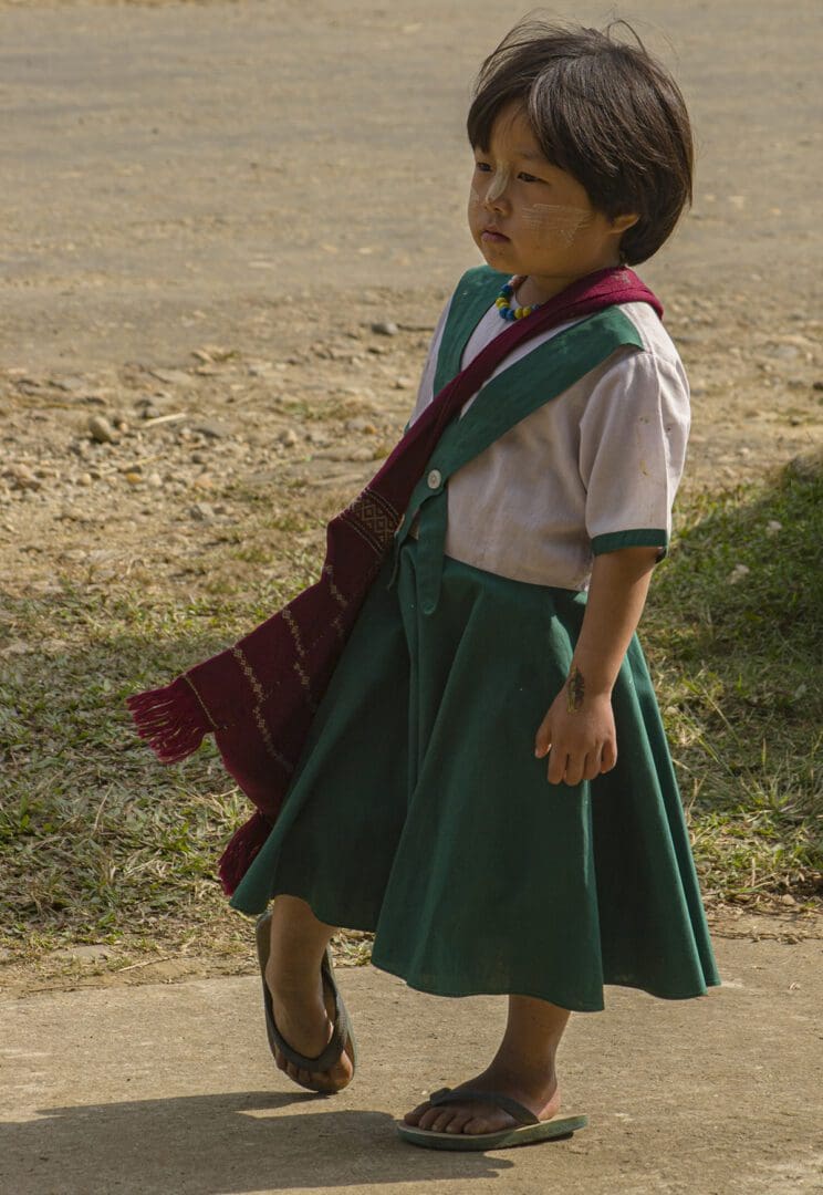 A little girl in a school uniform walking down the street.