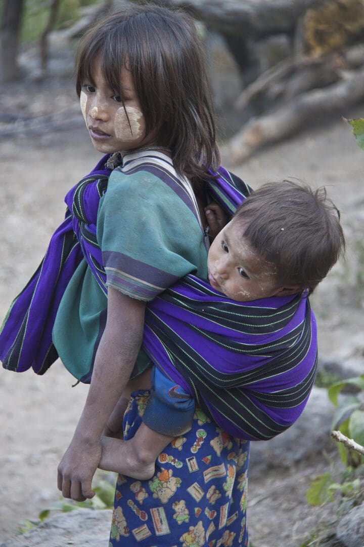 Two children carrying a child in a sling.