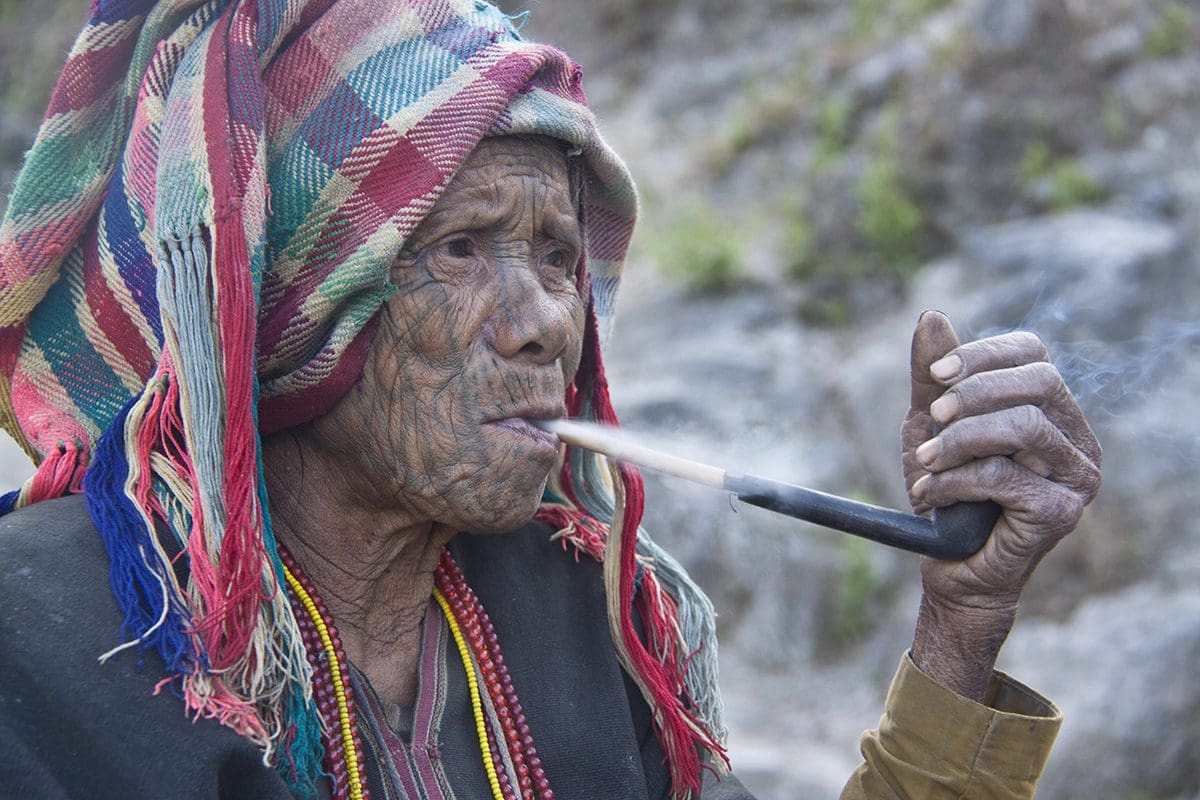An old woman smoking a pipe in the mountains.