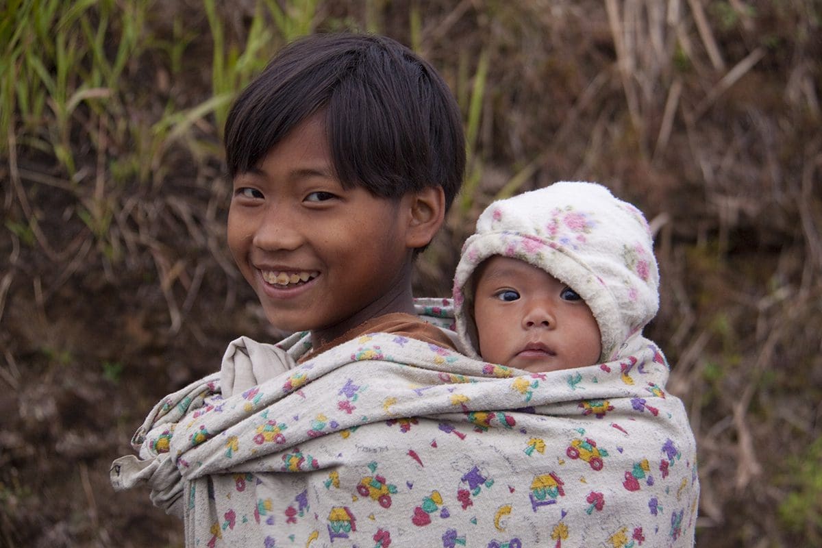 Two children in a sling holding a baby.