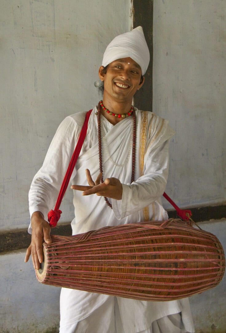 A man in a white robe holding a drum.