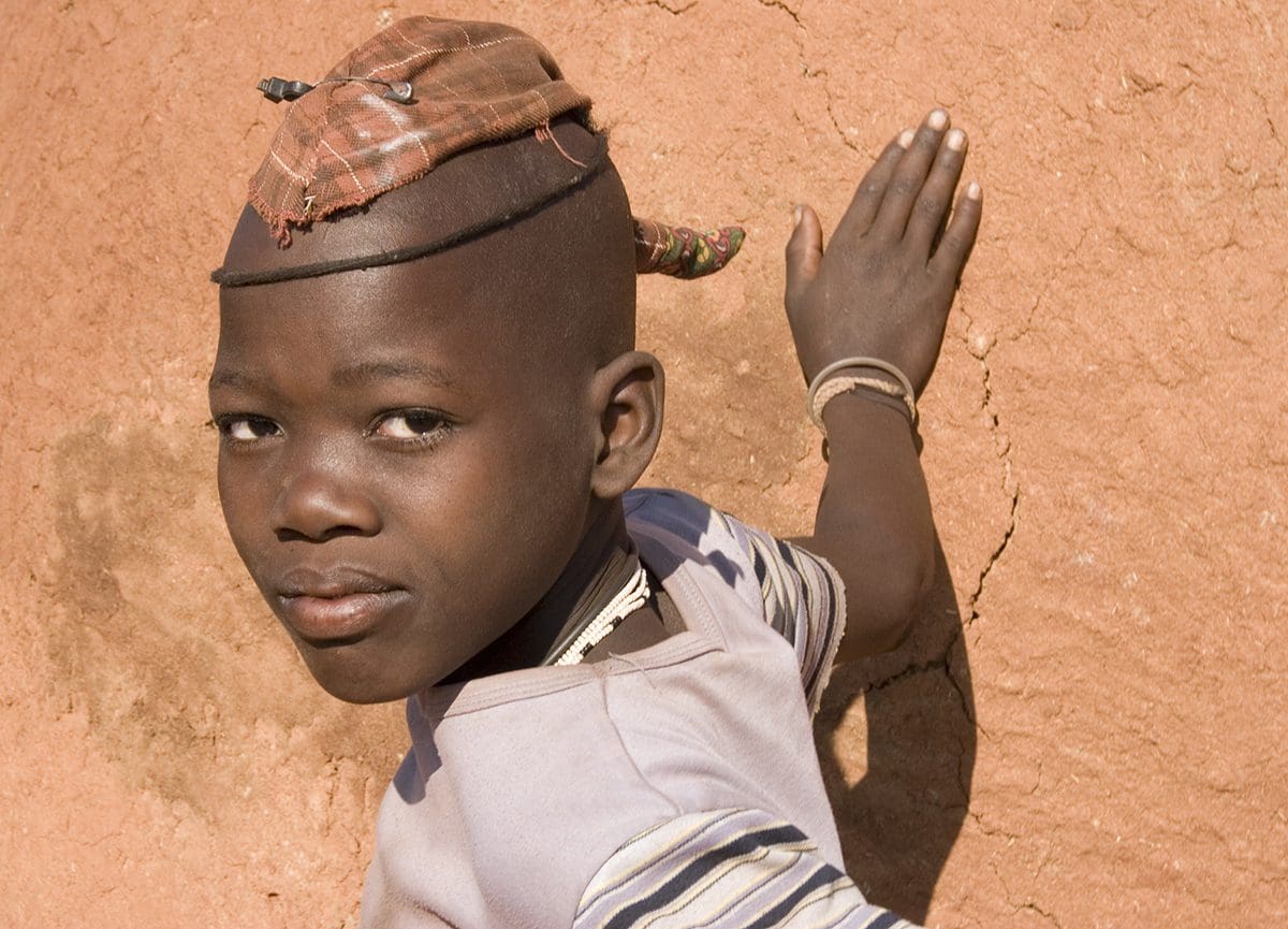 A boy wearing a hat leaning against a wall.