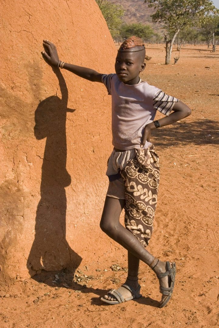 A boy standing next to a large rock in the desert.