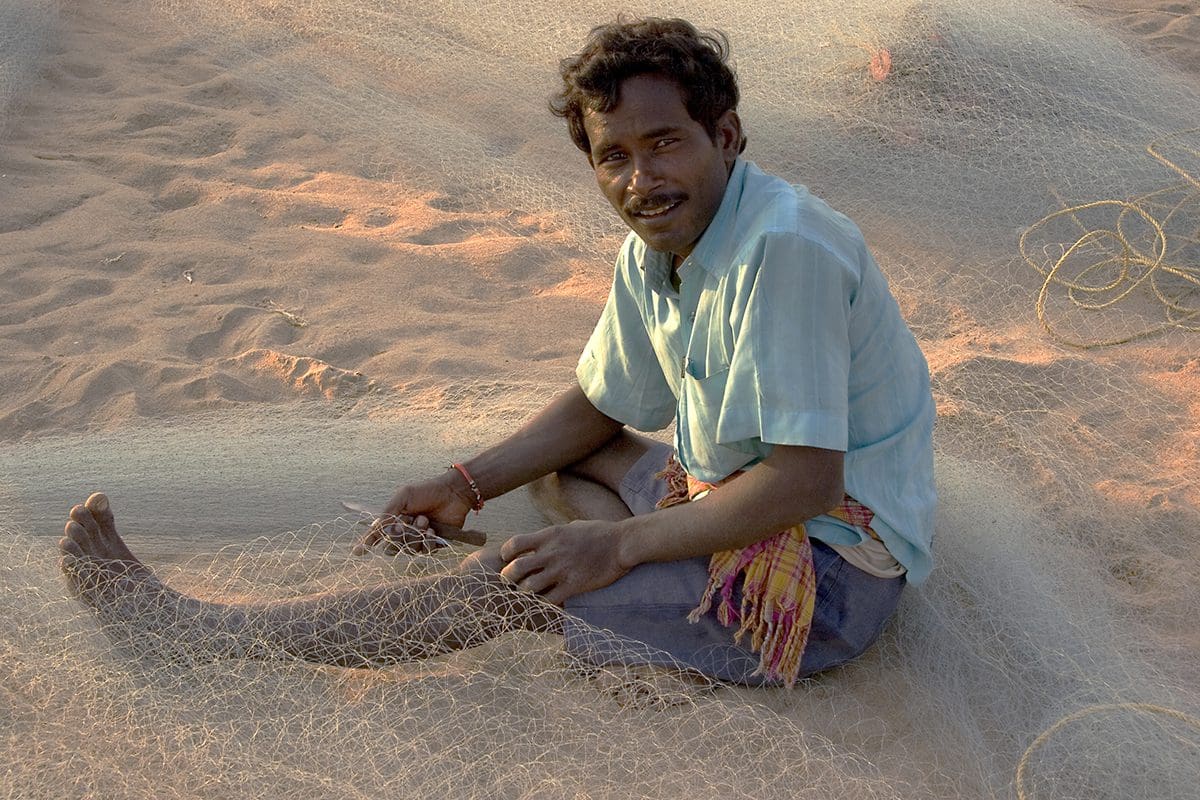 A man sitting on the sand with a fishing net.