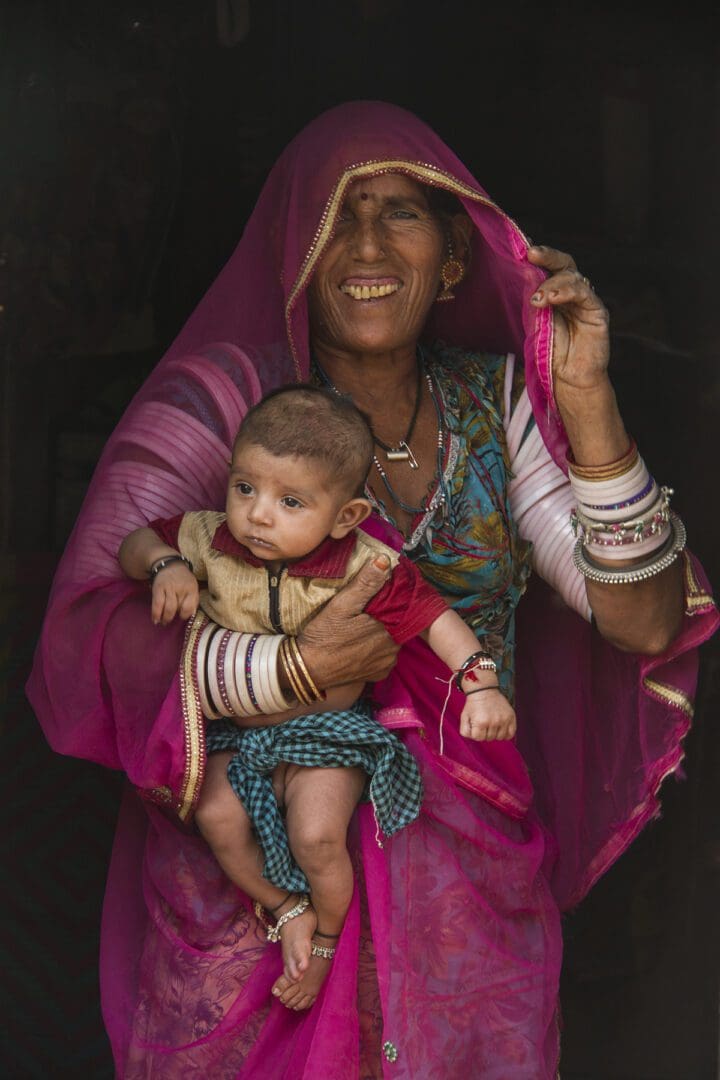 An indian woman holding a baby in a pink sari.