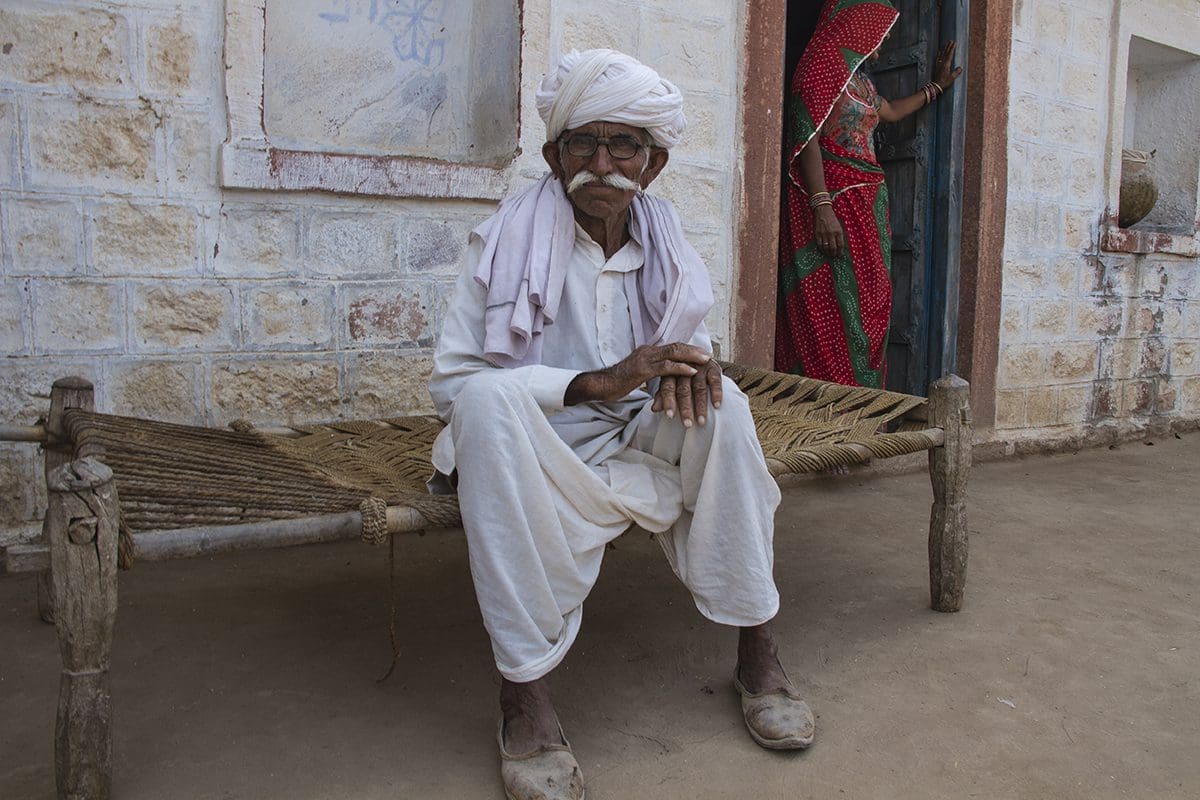 An indian man sitting on a bench next to a door.