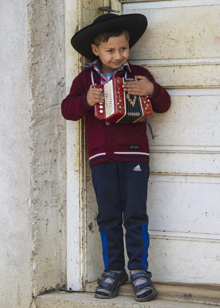 A young boy holding an accordion in front of a door.