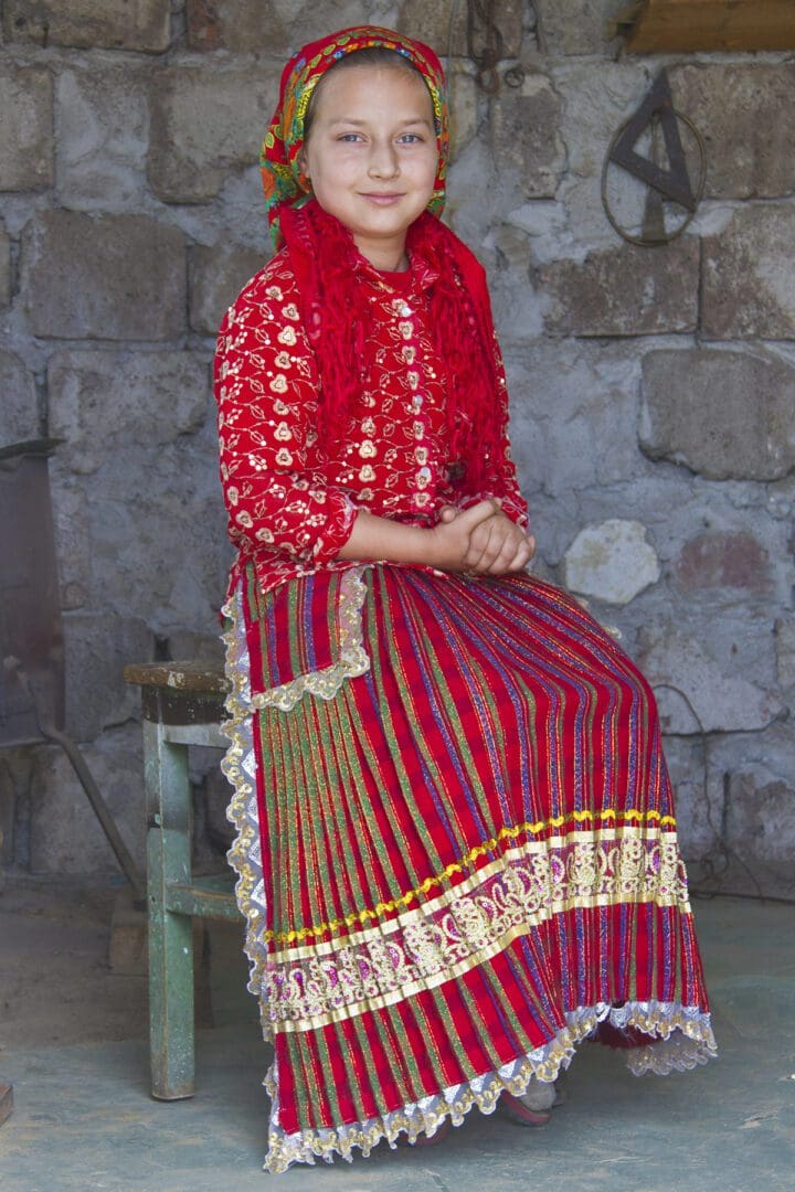 A girl in a traditional dress sitting on a stool.