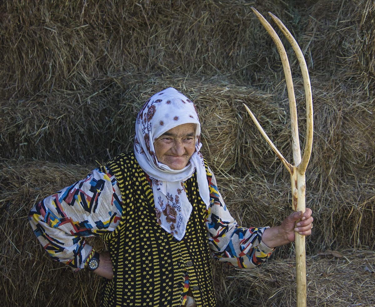 A woman holding a long stick in front of a pile of hay.