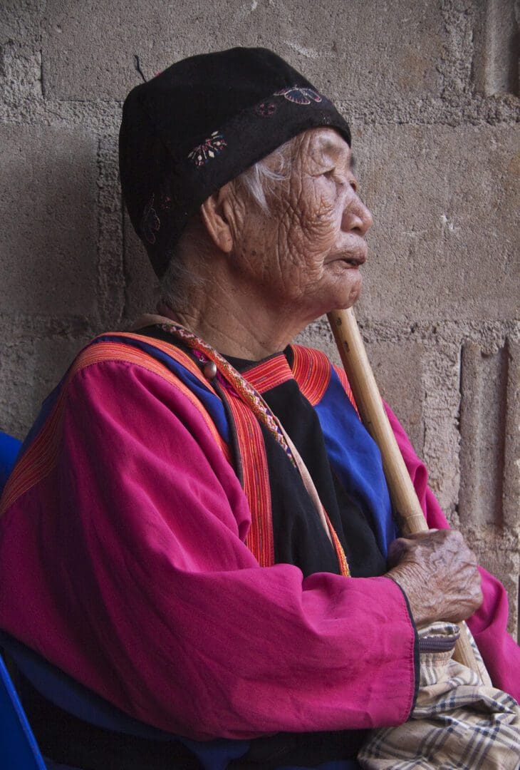 An old woman sitting on a wall with a wooden stick.