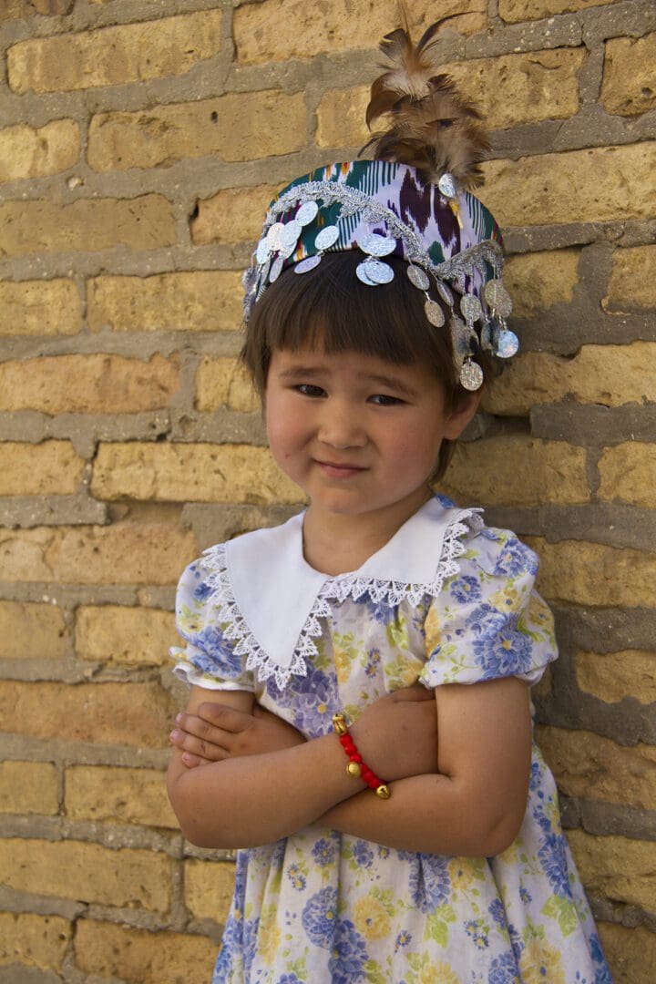 A little girl in a dress leaning against a brick wall.