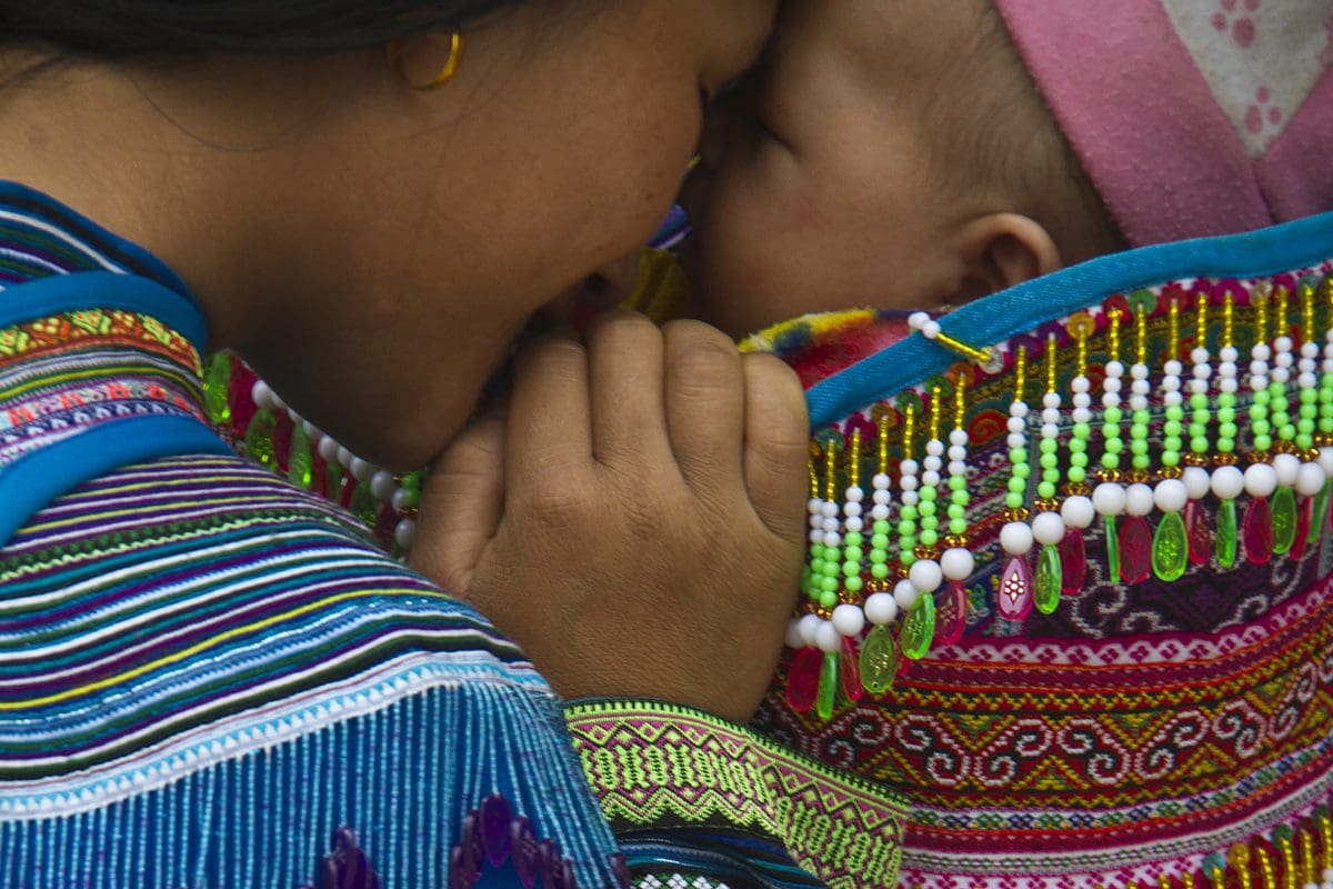A woman is holding a baby in a colorful sling.