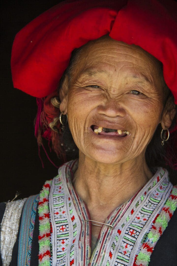 An old woman wearing a red hat and smiling.