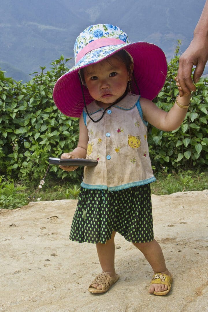 A little girl wearing a hat and holding a cell phone.