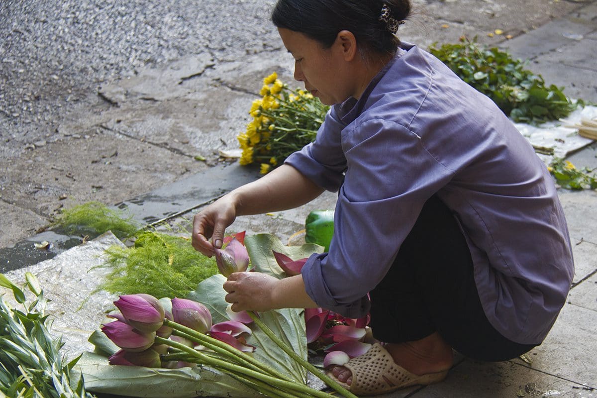 A woman kneeling on a sidewalk with flowers.