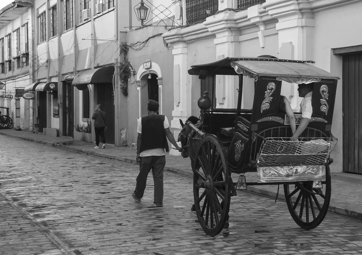 A black and white photo of a horse drawn carriage on a cobblestone street.