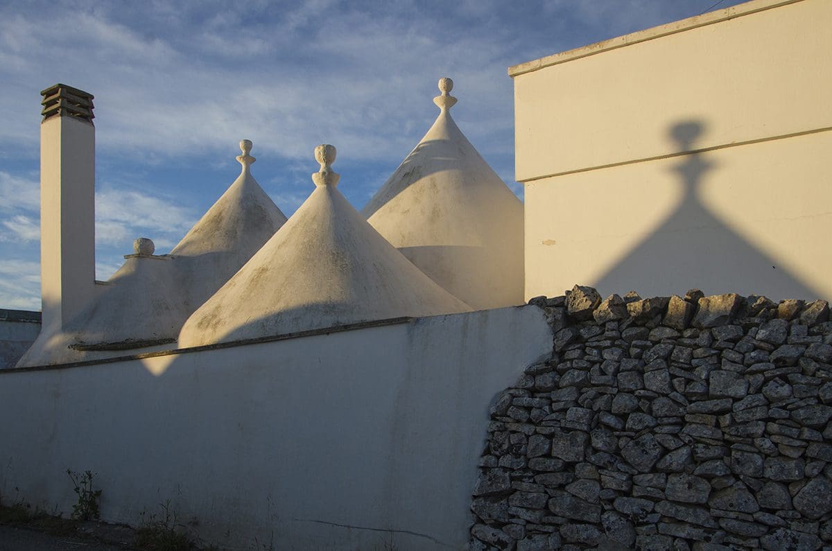 Shadows of trulli buildings on a stone wall.