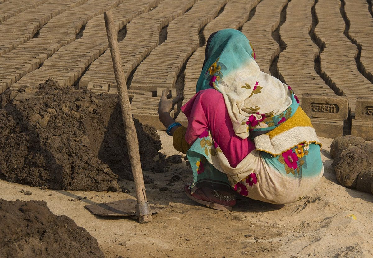 A woman in a sari working on bricks in a field.