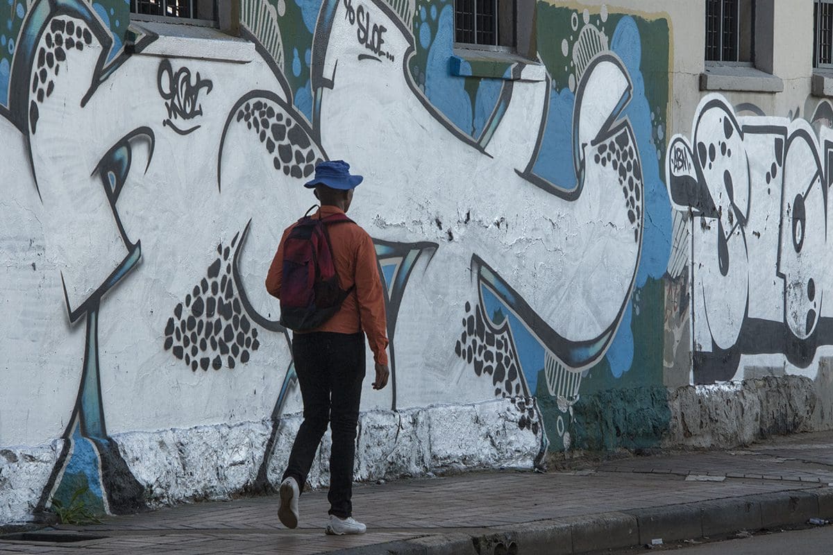 A man walking down a street with graffiti on the wall.